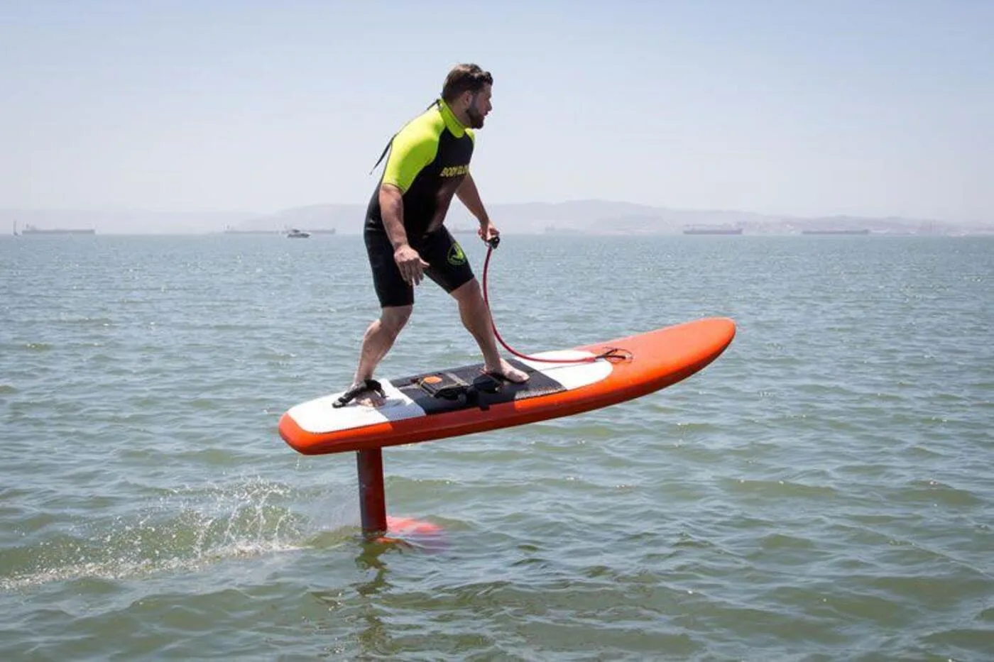 Rider foiling above the water on an orange board near cargo ships