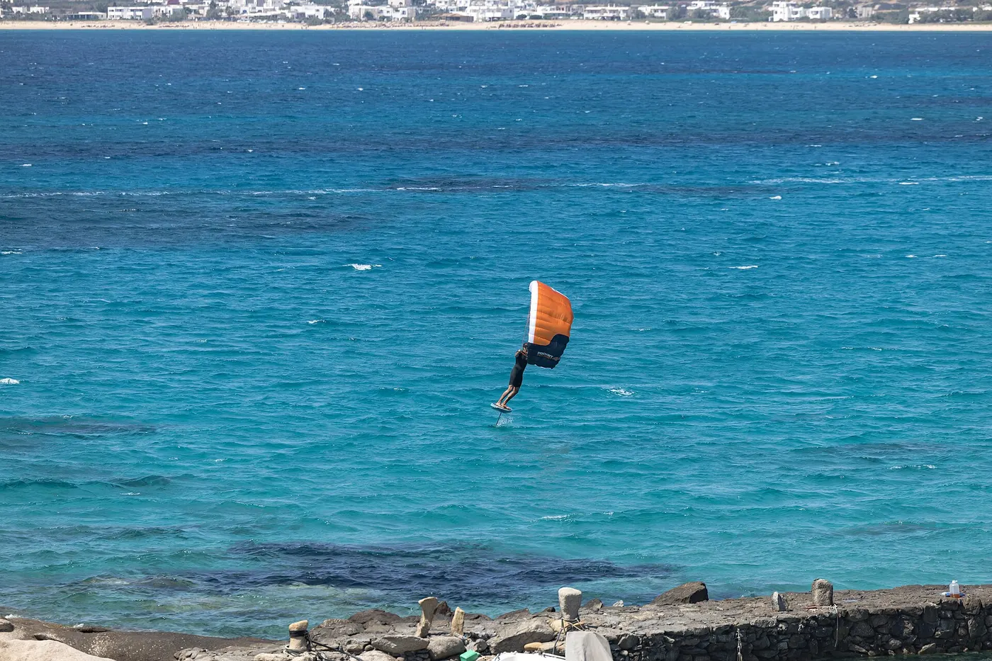 Wing foiler flying above blue water with an orange wing